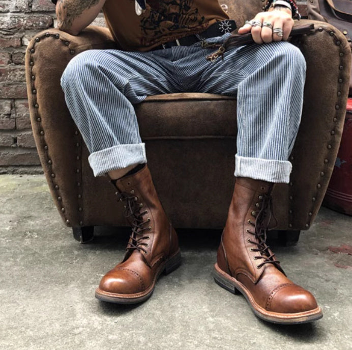 Person wearing brown leather boots sitting on a brown chair with a brick wall background