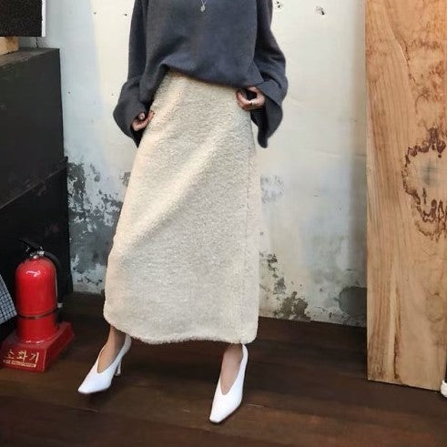 Person wearing a beige skirt and white shoes in a room with a wooden floor and wall.