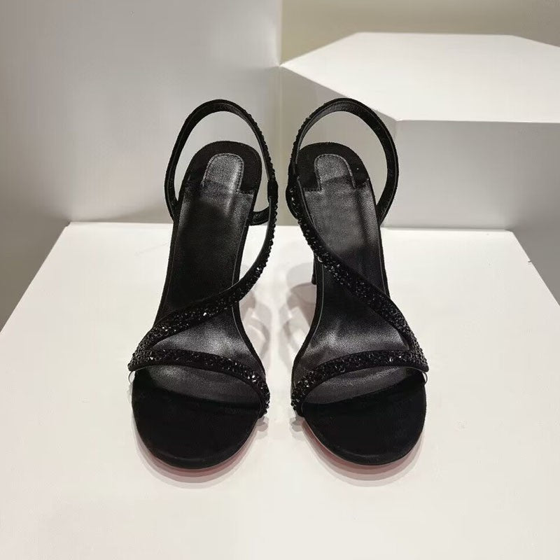 Pair of black high-heeled sandals with rhinestone details on a white platform.