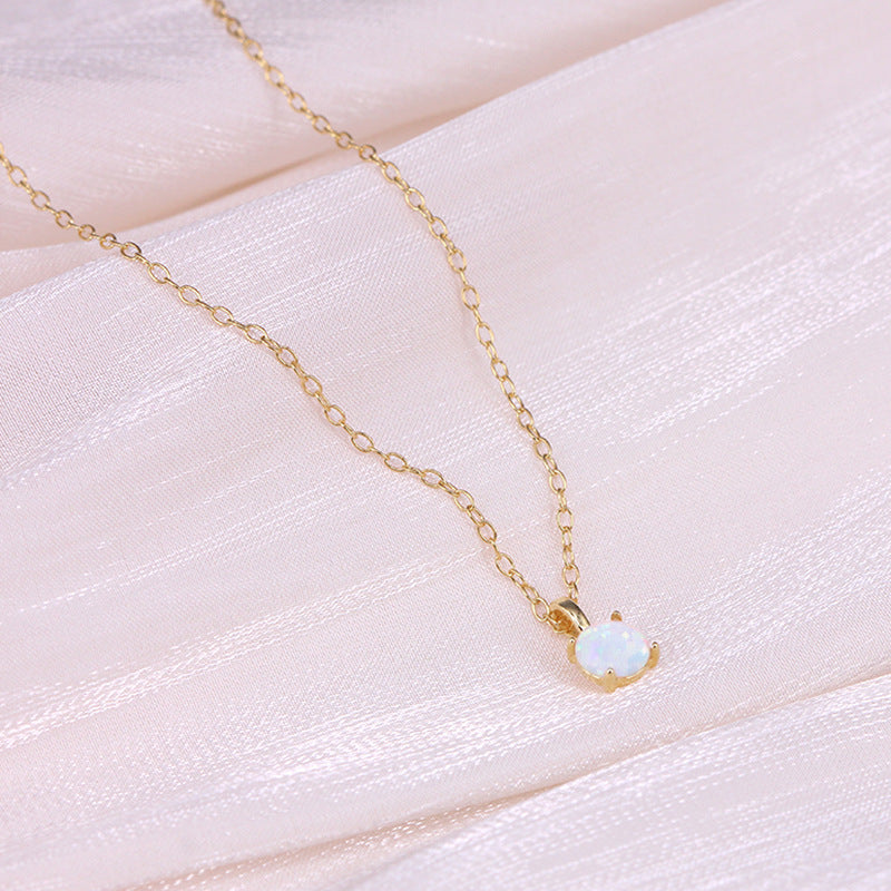 Gold necklace with a small opal pendant on a soft pink fabric background