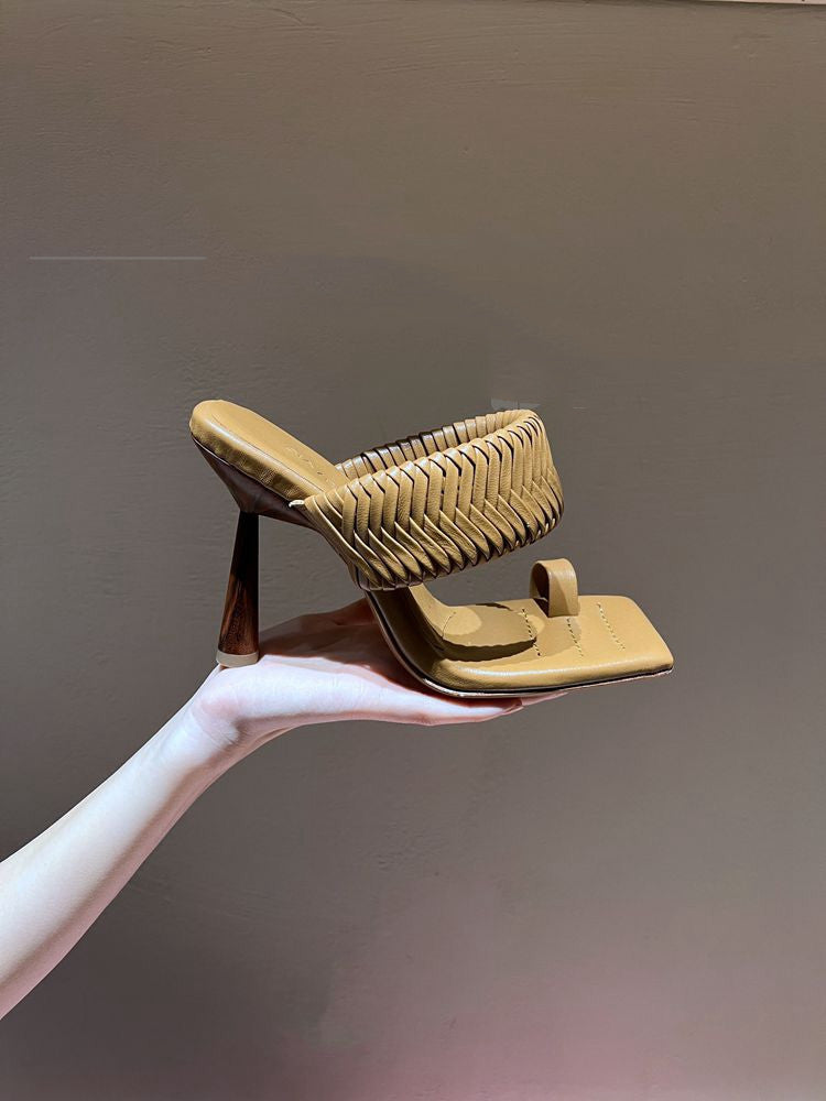 Hand holding a woven sandal against a plain background