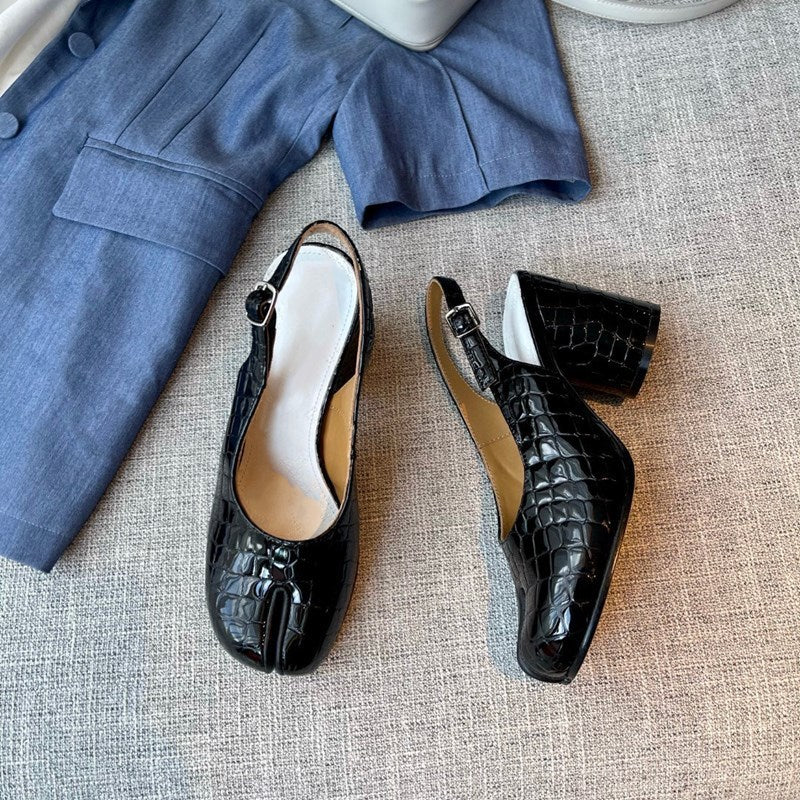 Black crocodile-patterned shoes on a textured surface with a blue outfit in the background.