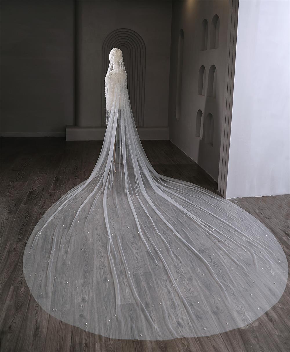 Long white wedding veil on a wooden floor with a dark wall and archway in the background