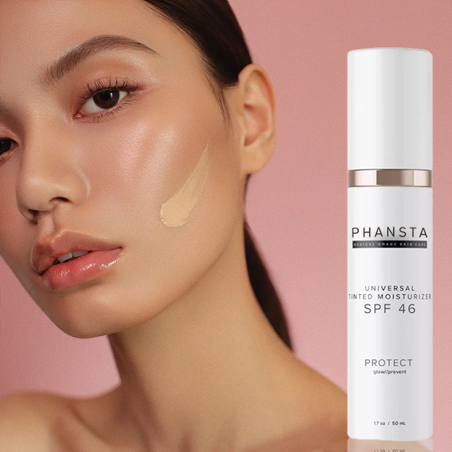 Woman with foundation on her face next to a PHANSTA sunscreen bottle on a pink background