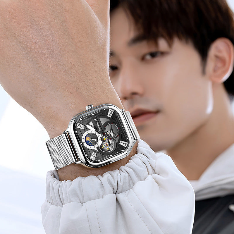 Person wearing a silver wristwatch with a detailed face, blurred background