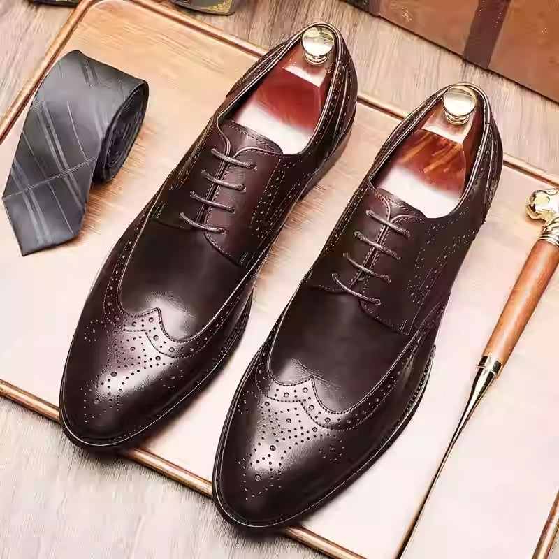 Pair of brown leather dress shoes on a wooden surface with a tie and other accessories.