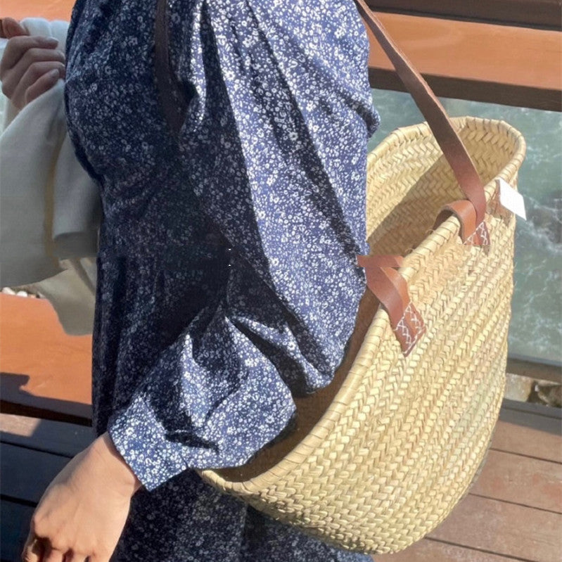 Person holding a straw bag with a blue floral dress in the background