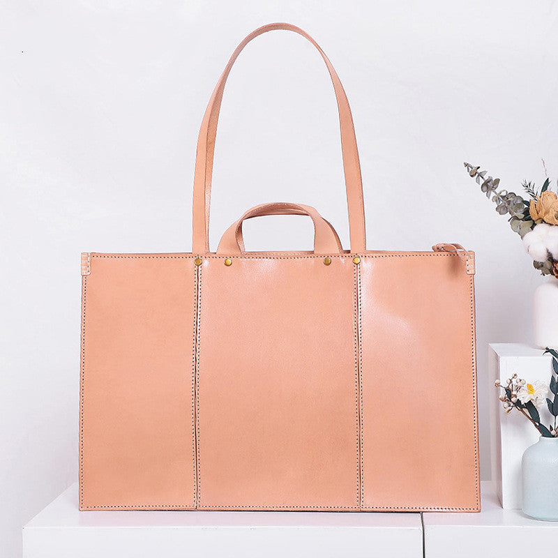 Tan leather tote bag on a white surface with a light background