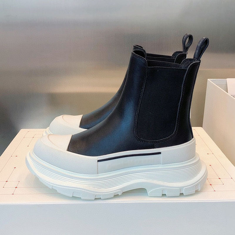 Black Chelsea boots with white soles on a light background