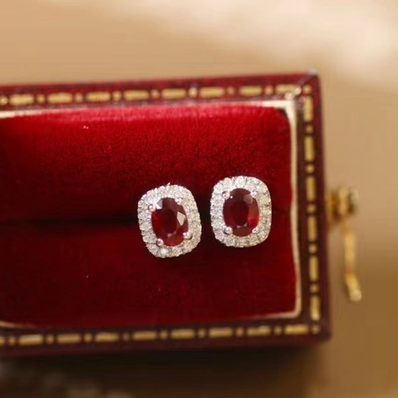 Pair of earrings with red gemstones on a red cushion in a jewelry box.