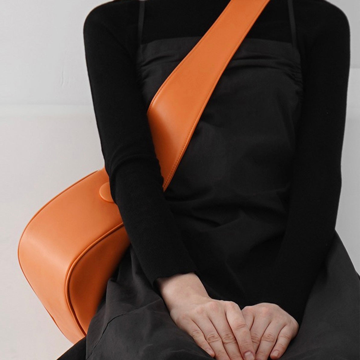 Person wearing a black outfit with an orange strap over their shoulder on a light gray background