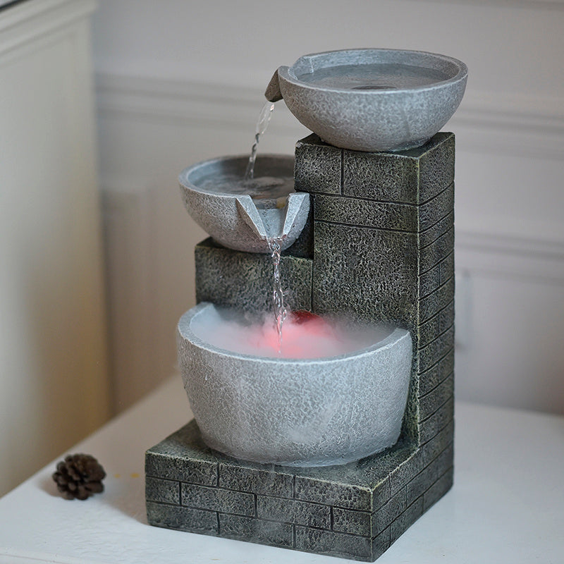 Decorative water fountain with three stone bowls on a white surface.
