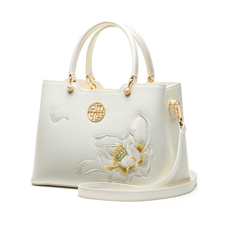 White handbag with floral embroidery and gold accents on a white background