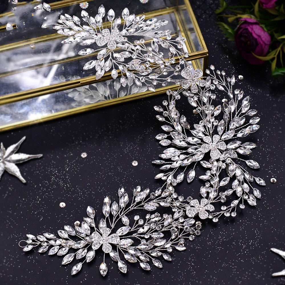 Silver leaf-shaped jewelry piece on a dark surface with a reflective background