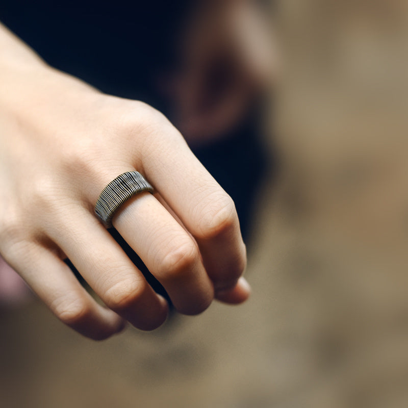 Hand wearing a textured ring with a blurred background