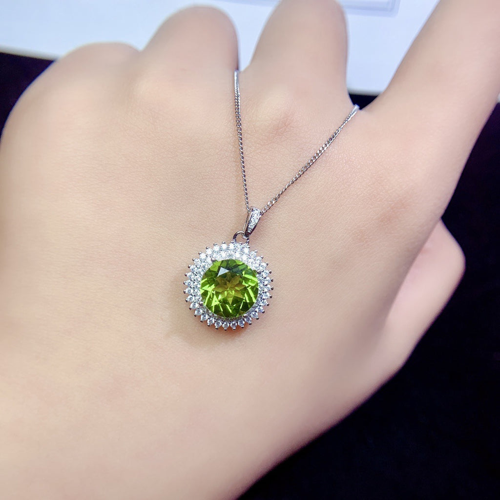Green gemstone pendant on a chain held in a hand against a neutral background
