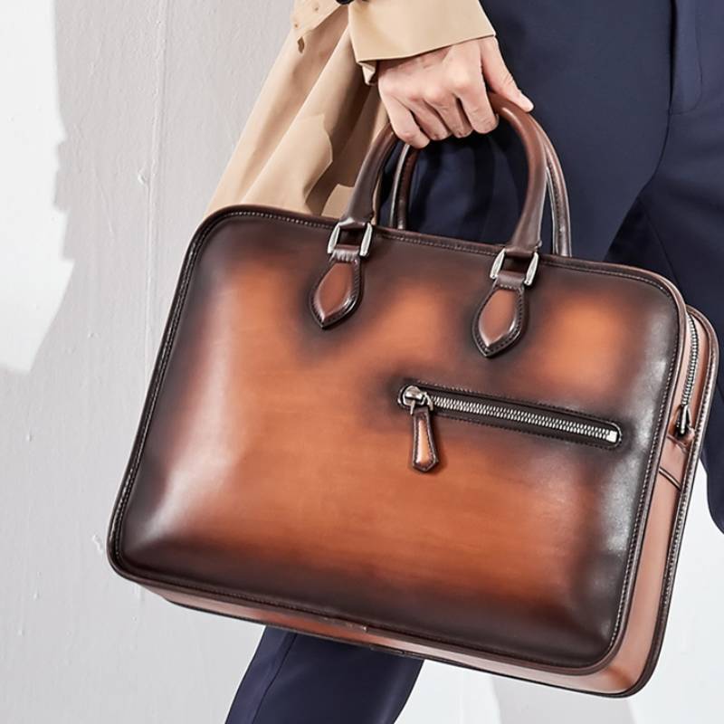 Brown leather briefcase held by a person wearing a beige coat and dark pants.