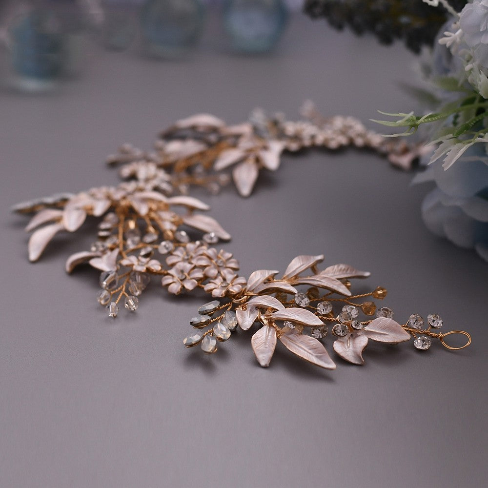 Gold and silver leafy jewelry piece on a gray surface with blurred floral background