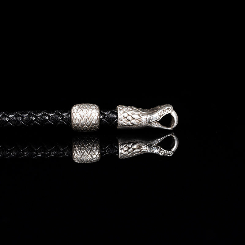 Silver snake head charm on a black braided cord against a black background