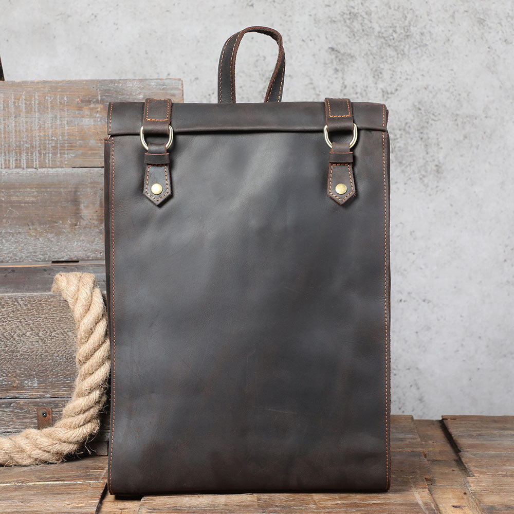 Dark leather backpack with brown straps on a wooden surface with a gray concrete wall background