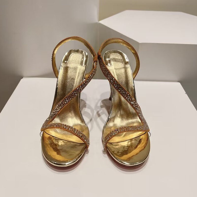 Pair of gold high-heeled sandals with rhinestone details on a white platform.