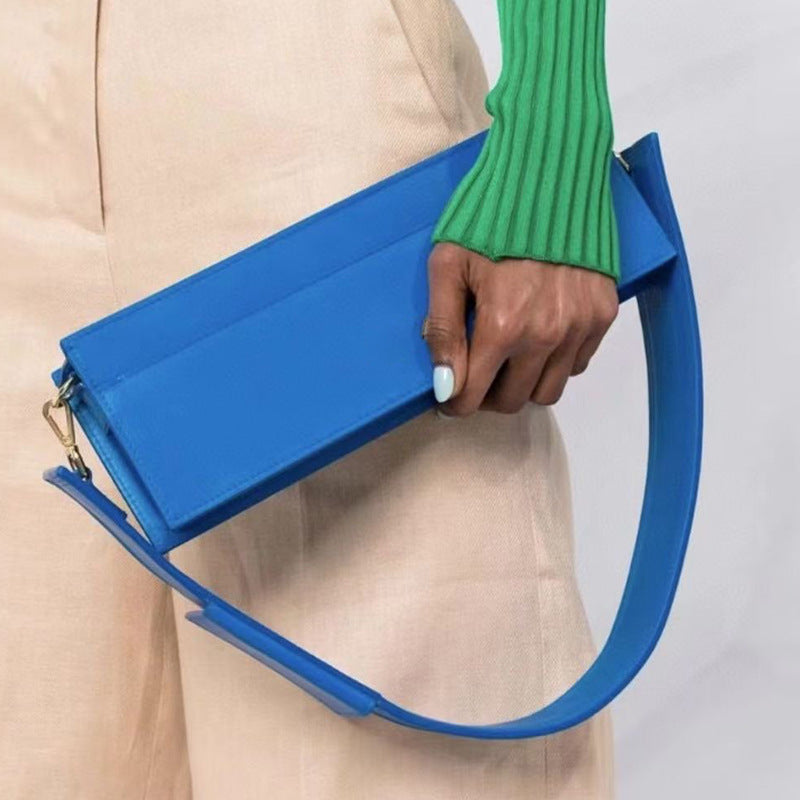Blue handbag held by a person wearing a green sweater and beige pants.