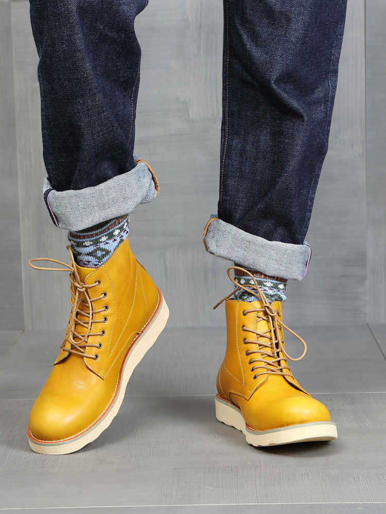 Yellow boots worn with rolled-up jeans on a neutral background