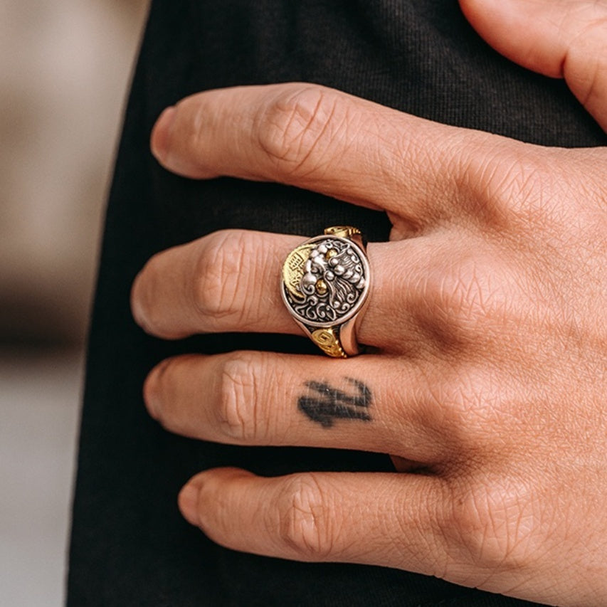 Hand wearing a gold and silver ring with intricate design on a blurred background