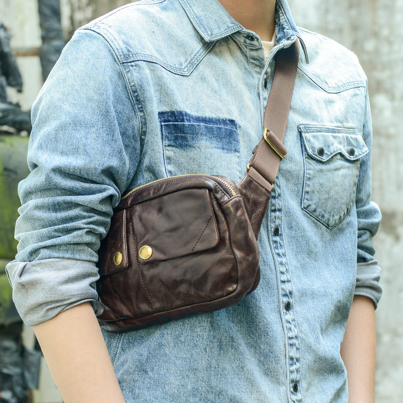 Person wearing a brown leather sling bag over a denim shirt