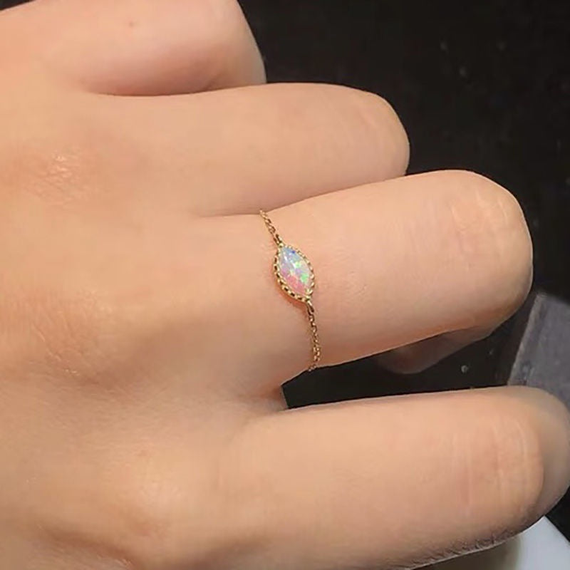 Gold ring with a colorful gemstone on a finger against a dark background