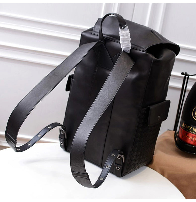 Black leather backpack on a white surface with a blurred bottle in the background