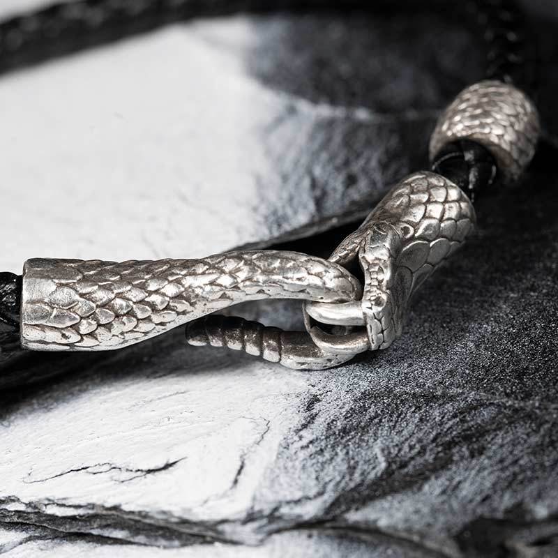 Silver dragon scale pendant on a leather cord against a stone background