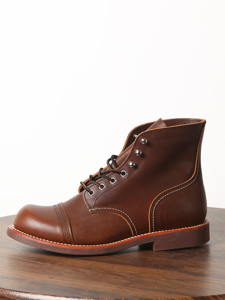 Brown leather boot on a wooden surface with a white background