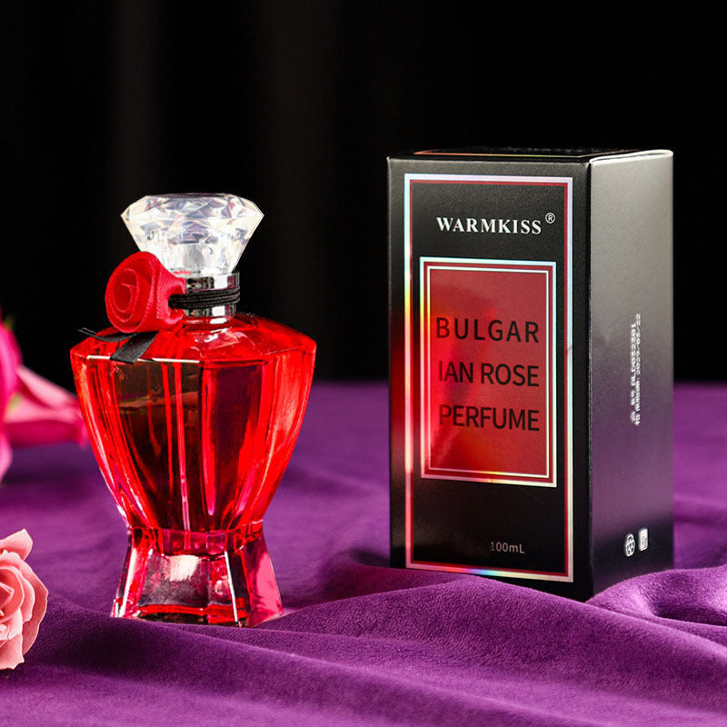Red perfume bottle with diamond-shaped cap and 'Warmkiss' packaging on a purple fabric background