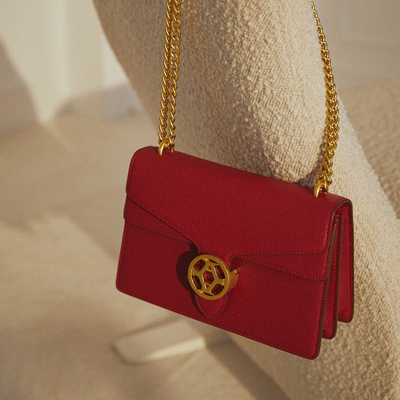 Red handbag with gold chain and emblem on a beige surface