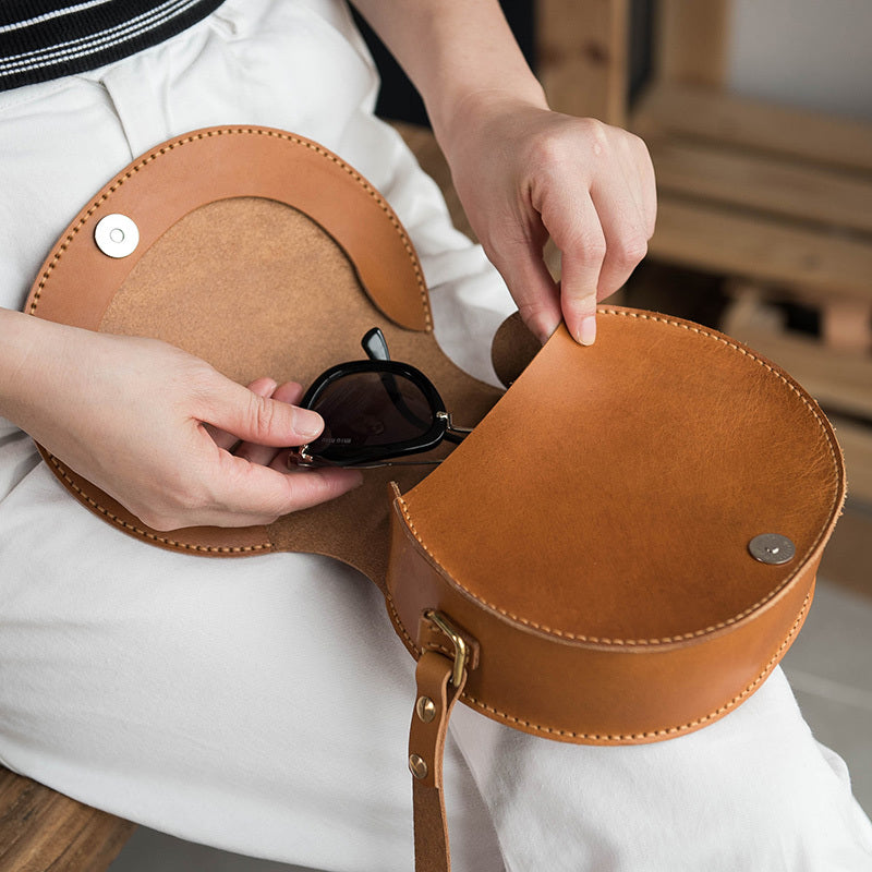 Person placing sunglasses into a brown leather handbag
