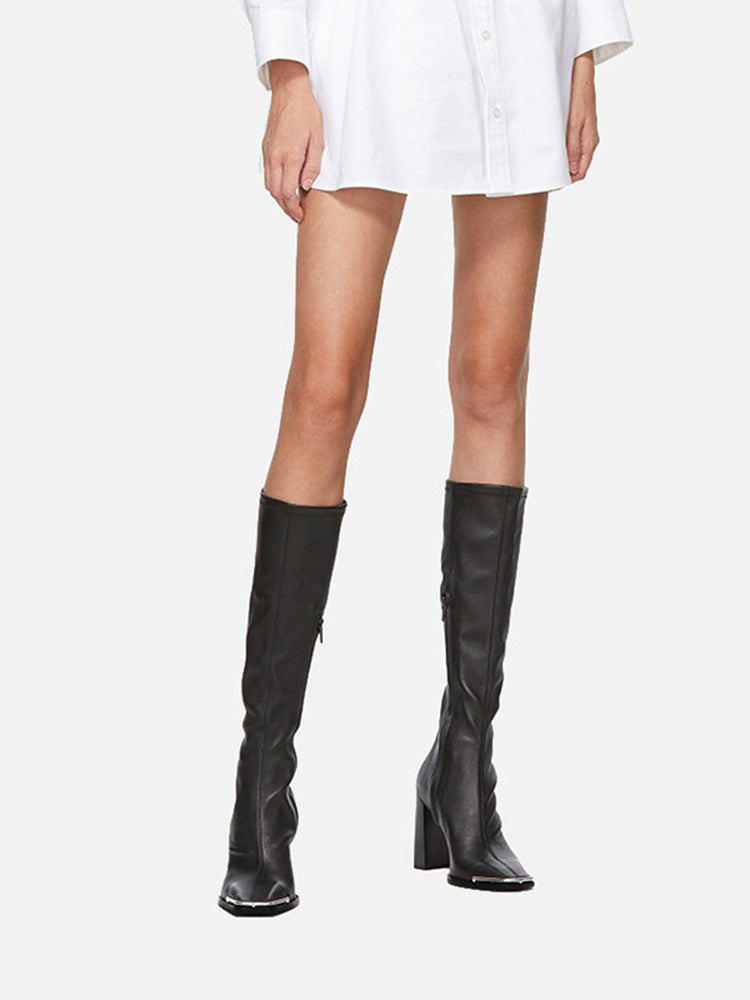 Black knee-high boots worn with a white outfit on a white background