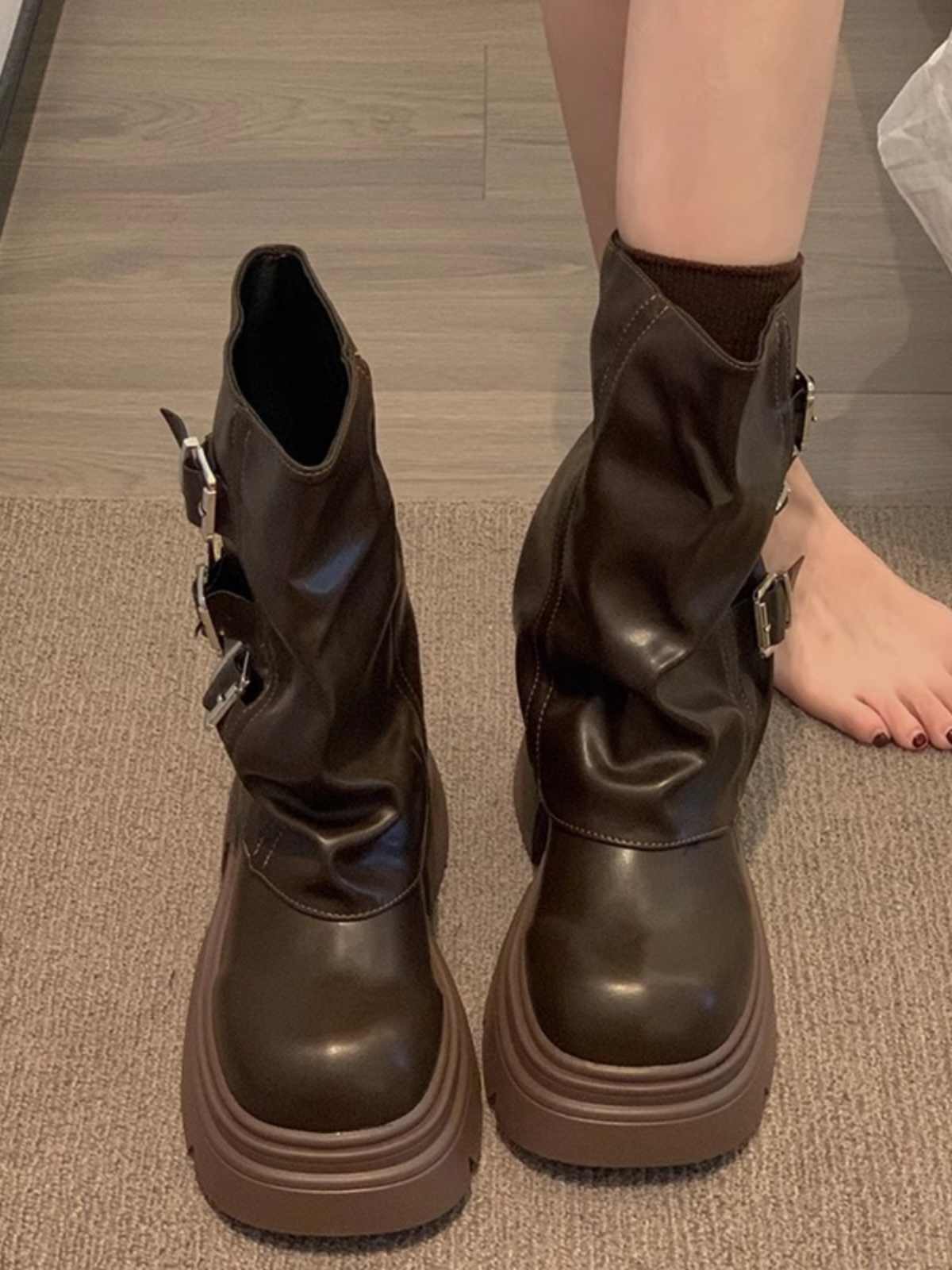Brown leather boots with buckles on a wooden floor.