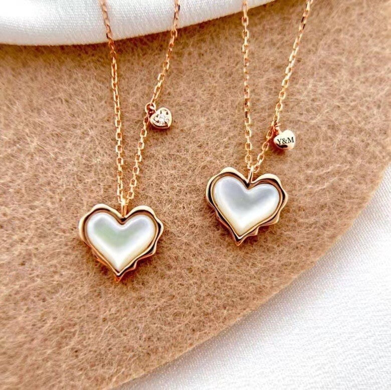 Two heart-shaped necklaces with gold chains on a beige surface.