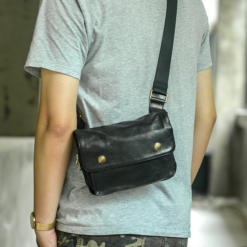 Person wearing a black leather crossbody bag with gold accents.