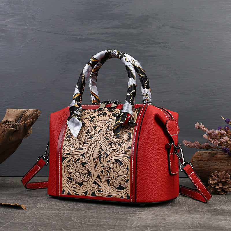 Red handbag with intricate leather design and patterned handle on a dark surface.