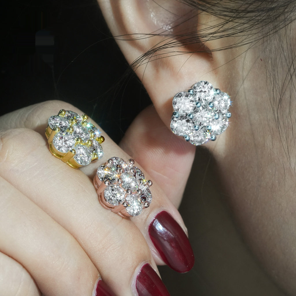 Close-up of a person wearing gold and silver floral earrings with red nail polish.