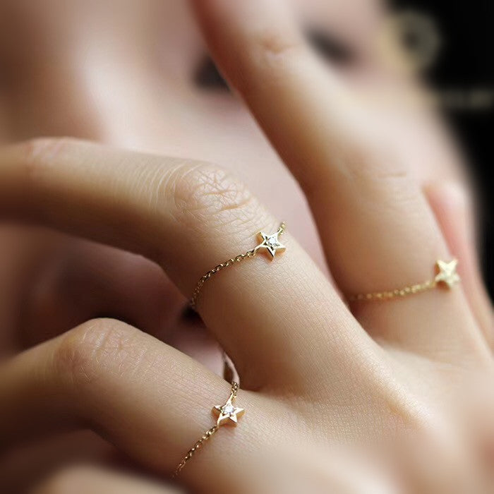 Close-up of a hand wearing two gold star-shaped rings on a blurred background