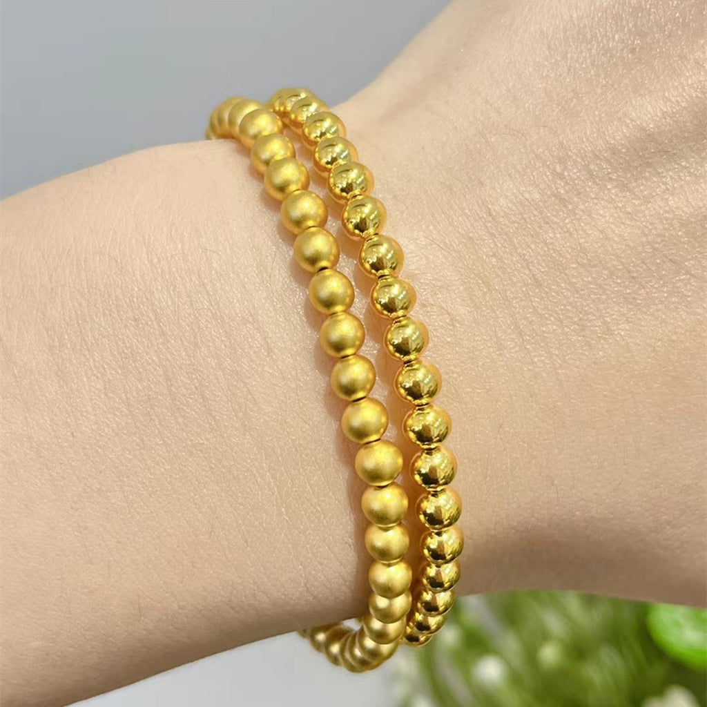 Gold beaded bracelet on a wrist with a neutral background