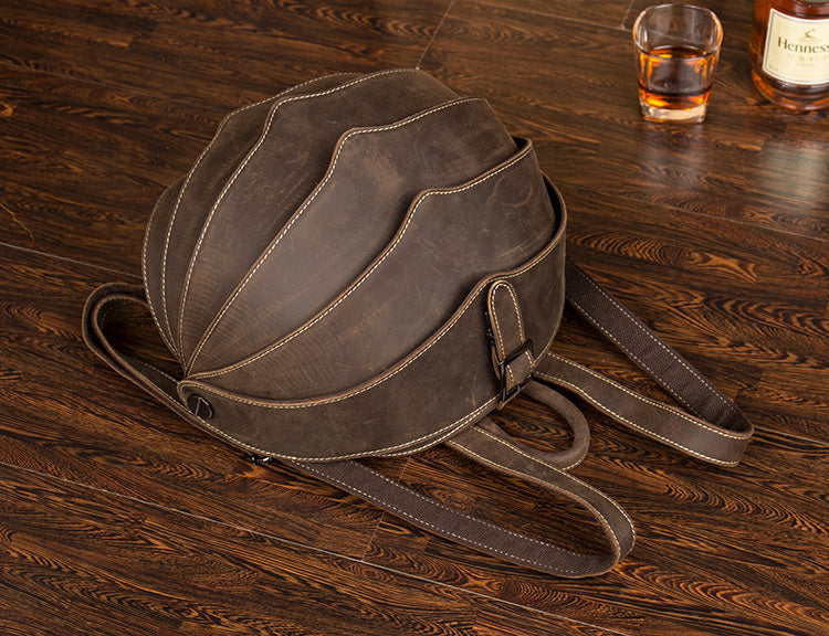 Brown leather backpack on a wooden surface with a glass of whiskey and bottle in the background.