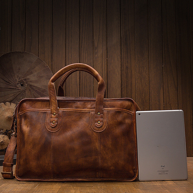 Brown leather briefcase next to a tablet on a wooden surface with a wooden panel background