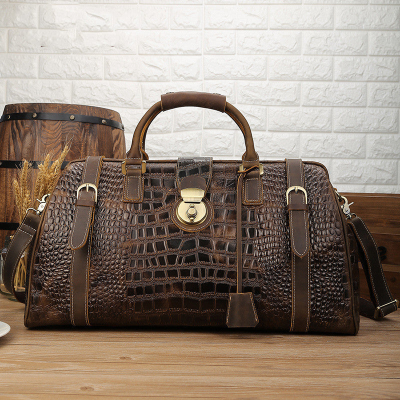 Brown leather bag with crocodile texture on a wooden surface with a white brick wall background.