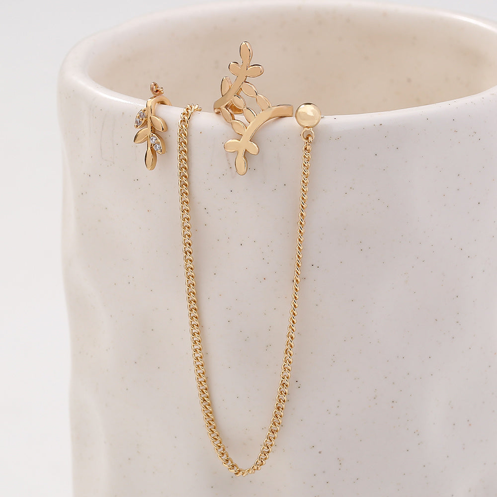 Gold chain earring and flower-shaped earring on a white ceramic cup