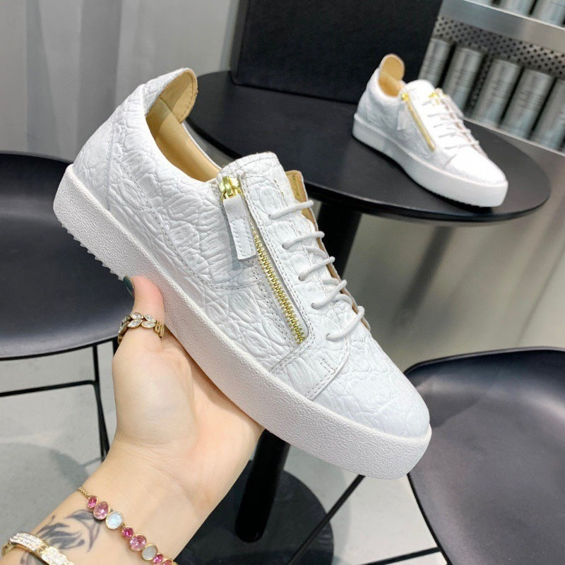 White sneaker with gold zipper held by a hand, with another sneaker in the background.