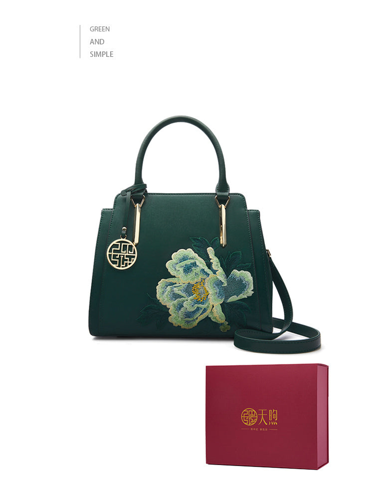 Green handbag with floral embroidery and matching red box on a white background